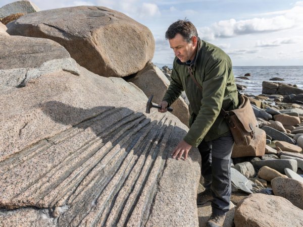 Geographer examining glacial striations on coastal granite boulders in natural light